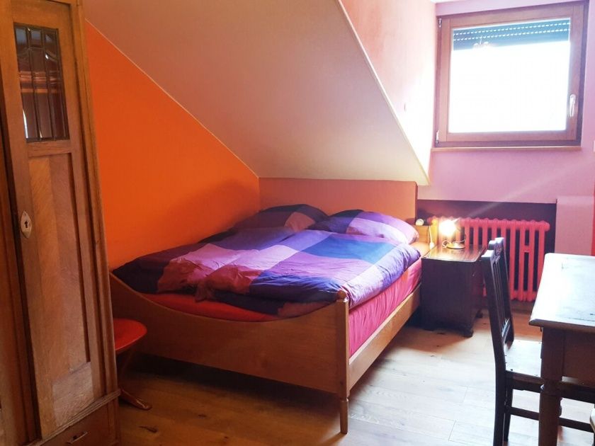 Das gemütliche, in sanfte Rot-Töne getauchte Schlafzimmer.  Moselblick, Eicheparkett und elektr. Rolladen. Dazu ein schöner alter Kleiderschrank. Bett 1.4 x 2 meter mit hochwertiger Matratze.